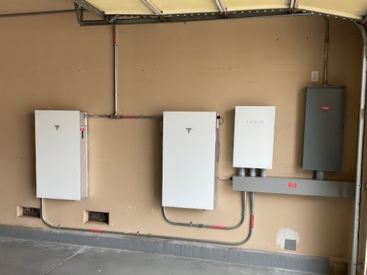 Two Tesla Powerwall 3 batteries mounted on a garage wall beside the gateway and main electrical panel.